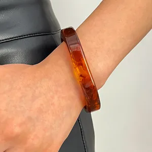 Close-up of vintage amber smudge resin bangle on model's wrist with leather background