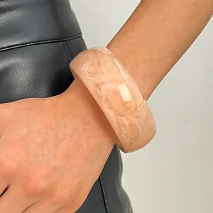 Close-up of a wide marbled resin bangle with retro peach tones worn on a model's wrist