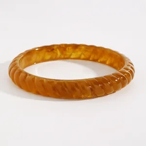 Close-up of amber resin bangle showing marbled texture and twisted design.