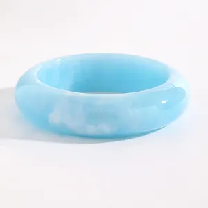 Close-up of a wide light blue resin bangle with white marble textures and glossy finish.