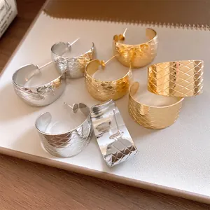 Nahaufnahme von C-förmigen Metallohrringen mit Rautenmuster in Gold und Silber.
