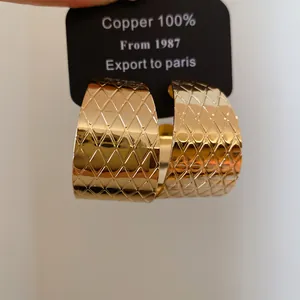 Detailansicht goldene C-förmige Metallohrringe mit Rautenmuster-Prägung.
