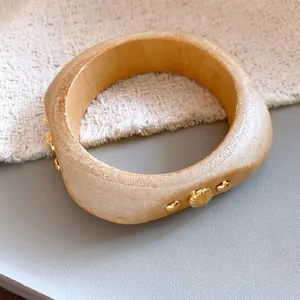 Makro-Detail eines Armreifs aus Naturholz mit goldenen Nieten und organischer Textur