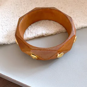 Nahaufnahme eines facettierten Holzarmreifs mit eleganten goldfarbenen Metallnieten