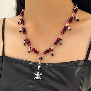 Detailopname van een punk ketting met rood-zwarte kralen en zilveren doodskop hanger