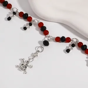 Detail van een punk Y-vormige ketting met rode en zwarte kralen en een schedelhanger.