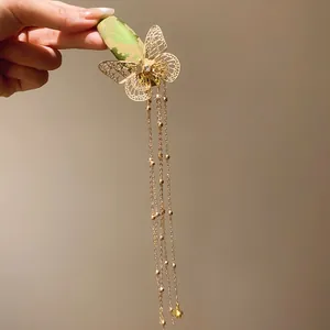 Detailed view of gold butterfly hair clip with green embroidery and long tassels