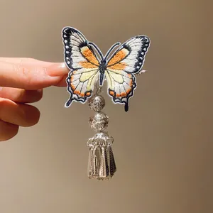Detailed view of vintage butterfly embroidery hair clip with silver tassel and bell charm