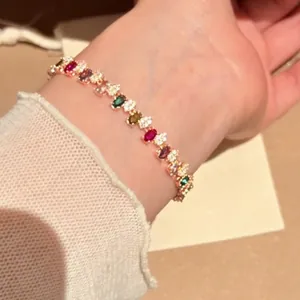 Elegantes goldfarbenes Armband mit unregelmäßigen bunten Regenbogensteinen am Handgelenk.