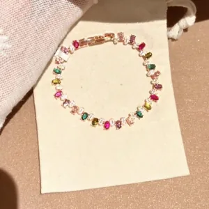 Detailansicht eines bunten Regenbogen-Edelsteinarmbands auf einem beigen Stoffbeutel
