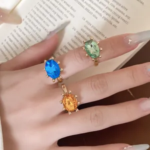 Nahaufnahme von drei bunten ovalen Strassringen auf der Hand mit Buchhintergrund