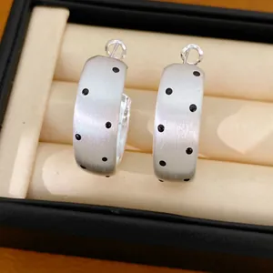 Gros plan détaillé de boucles d'oreilles créoles en argent brossé avec des pois noirs