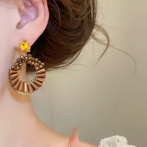 Nahaufnahme von Kristall-Creolen mit plissiertem Metall-Fächerdesign an einem Modell.