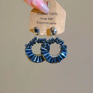 Detailansicht eleganter blauer Perlenohrringe mit facettierten Kristallsteckern auf Karte.