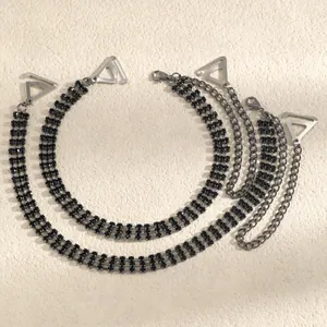 Detailed view of black rhinestone bra straps with silver triangle clips on beige surface.