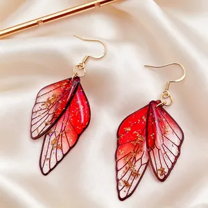 Primer plano de pendientes de hada con forma de ala de mariposa roja y detalles de pan de oro