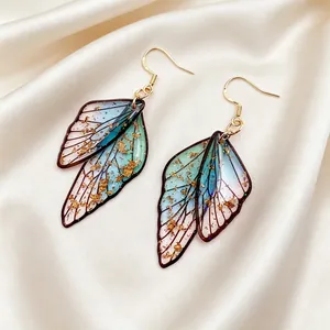 Detalle de pendientes con forma de alas de mariposa traslúcidas y pan de oro