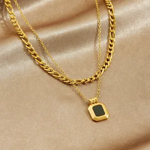 Dettaglio di una collana a doppio strato placcata oro con catena Figaro e ciondolo nero vintage.