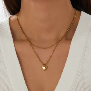 Vista dettagliata di una collana a strati placcata in oro con ciondolo a cuore su una modella.