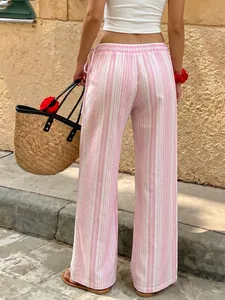 Back view of pink striped wide-leg trousers in a casual resort setting with straw bag