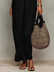 Lower body detail of a black summer vacation dress paired with a woven straw bag