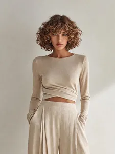 Dettaglio completo beige: top asimmetrico incrociato e pantaloni larghi con tasche.