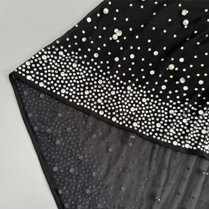 Macro view showing shimmering gradient rhinestones and pearls on black mesh evening dress