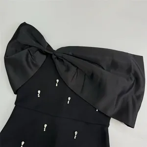Detail of a black bandage dress with a large satin bow and teardrop crystal accents.
