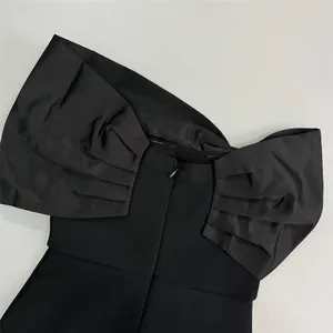 Close-up of black off-shoulder bandage dress with oversized ruffle details and zipper.