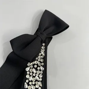 Détail d'une robe bandage noire avec un nœud élégant et des ornements en strass brillants.