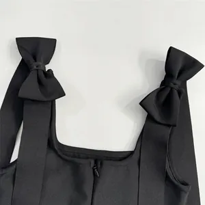 Détail d'une robe bandage noire montrant les bretelles à nœuds et la texture du tissu côtelé