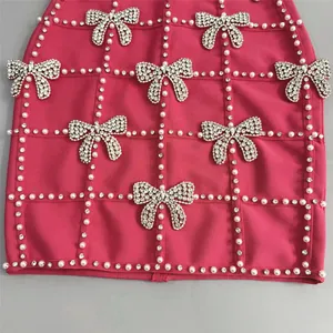 Close-up detail of a pink bandage dress featuring crystal bow ties and a white pearl grid pattern