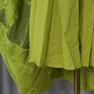 Detailed view of green embroidered lace fabric and pleated inner lining of a summer dress.