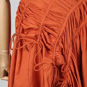Dettaglio ravvicinato di un abito arancione arricciato con coulisse e decori a fiocco