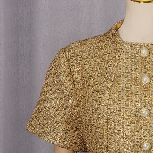 Gros plan sur la texture du tweed doré et les boutons de perles décoratifs de cette robe