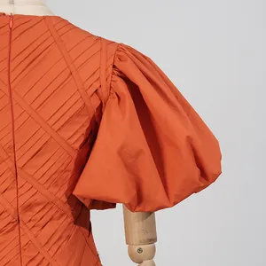 Dettaglio della manica a sbuffo e del tessuto plissettato su un abito color arancio