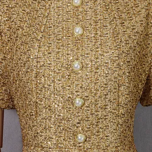 Gros plan sur le tissu en tweed doré rétro et les boutons de perles élégants de la robe.