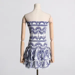 Vista trasera de minivestido palabra de honor blanco con bordado azul y bajo de volantes.