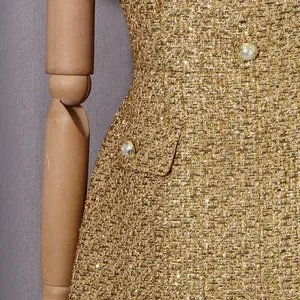 Gros plan sur le tissu en tweed doré luxueux et les boutons perlés élégants d'une robe.
