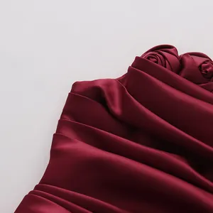 Detail view of wine red satin tube dress showing exquisite 3D fabric roses and pleated texture.
