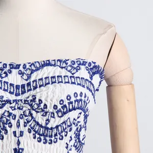Detalle del intrincado bordado floral azul en un minivestido blanco sin tirantes fruncido