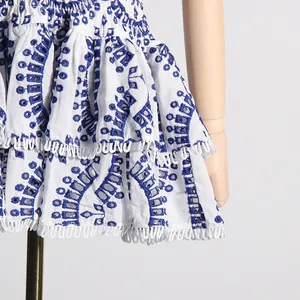 Detalle de vestido playero blanco con bordado azul y dobladillo con volantes y ojales