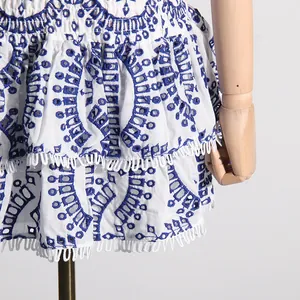 Detalle de cerca de un vestido corto bohemio blanco con bordados azules y ribetes de flecos