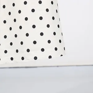 Primo piano del dettaglio di un abito bianco stile francese con stampa a pois neri.