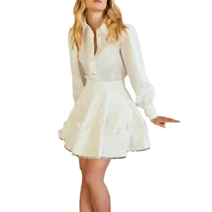 Elegante conjunto de camisa blanca de manga larga y minifalda texturizada con flecos.
