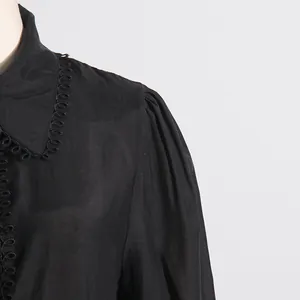 Primer plano del hombro de una camisa negra con pliegues elegantes y un ribete de lazos