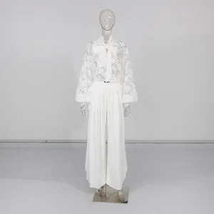 Dettaglio dell'elegante completo con camicetta in pizzo bianco e pantaloni larghi