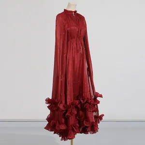 Vista detallada de un vestido de gala rojo con diseño de capa y textura de volantes en el bajo.