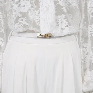 Dettaglio di camicetta in pizzo bianco e pantaloni larghi con cintura fibbia dorata.