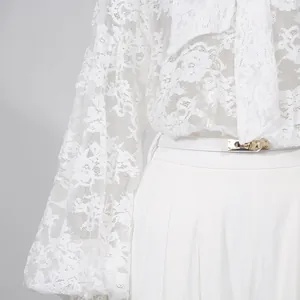 Dettaglio della maglia in pizzo con fiocco e pantaloni larghi con fibbia dorata